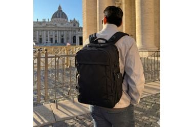 A traveler wearing the EVERKI ONE backpack in a sunlit city square
